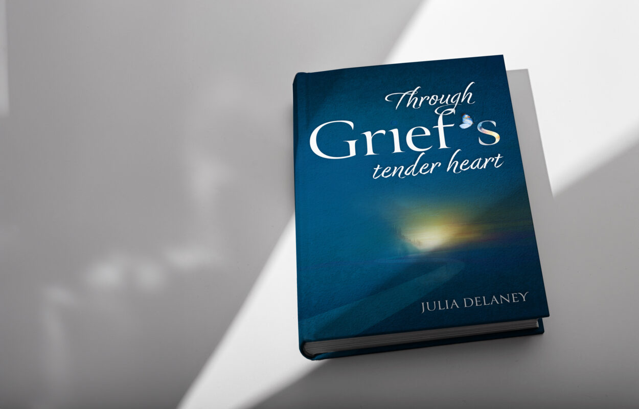 Through Grief's Tender Heart book by Julia Delaney. a book cover. The cover is predominantly a deep blue color that transitions from a darker shade at the top to a lighter tone at the bottom. There's a spotlight effect on the cover, highlighting the title and part of the image on the cover